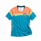 Fronte della maglia away dell'Australia 2026 turchese con spalle sfumate oro e arancione e stemma sul petto
