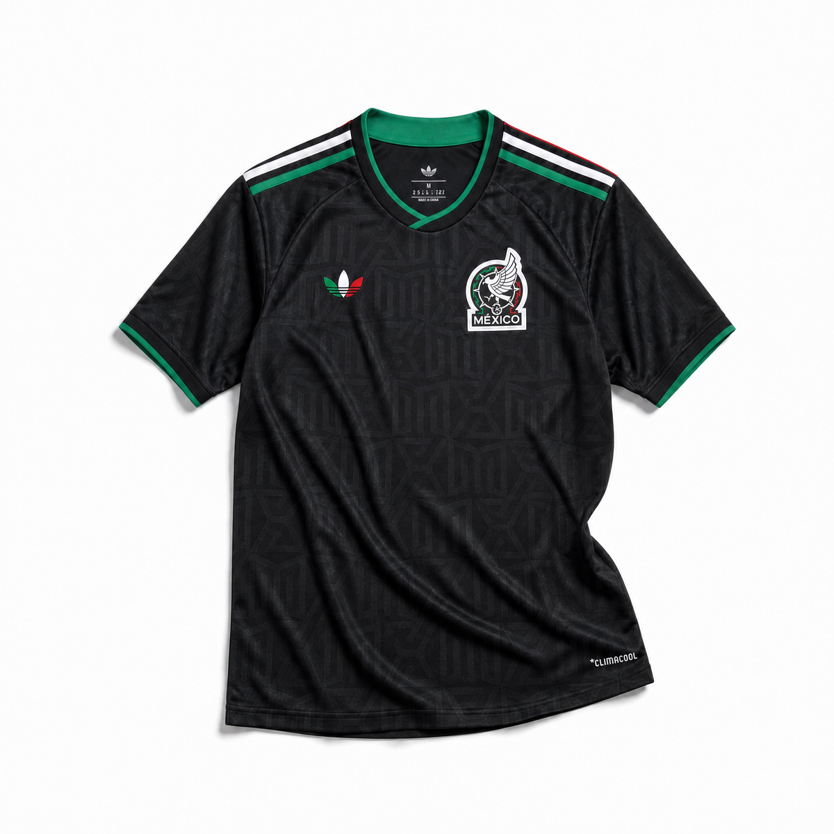 Maglia third Messico Coppa del Mondo 2026 — vista frontale su superficie in legno, colore nero con pattern geometrico azteco tono su tono, colletto rotondo con bordino tricolore verde-bianco-rosso e stemma nazionale sul petto sinistro